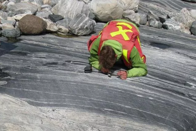 Master i geologi med berggrundsinriktning. Man som studerar berggrunden med lupp.